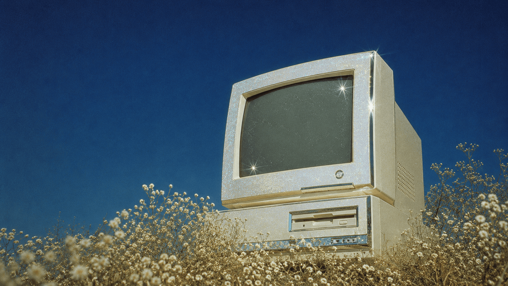 A vintage Macintosh computer standing in wildflowers under a deep blue sky