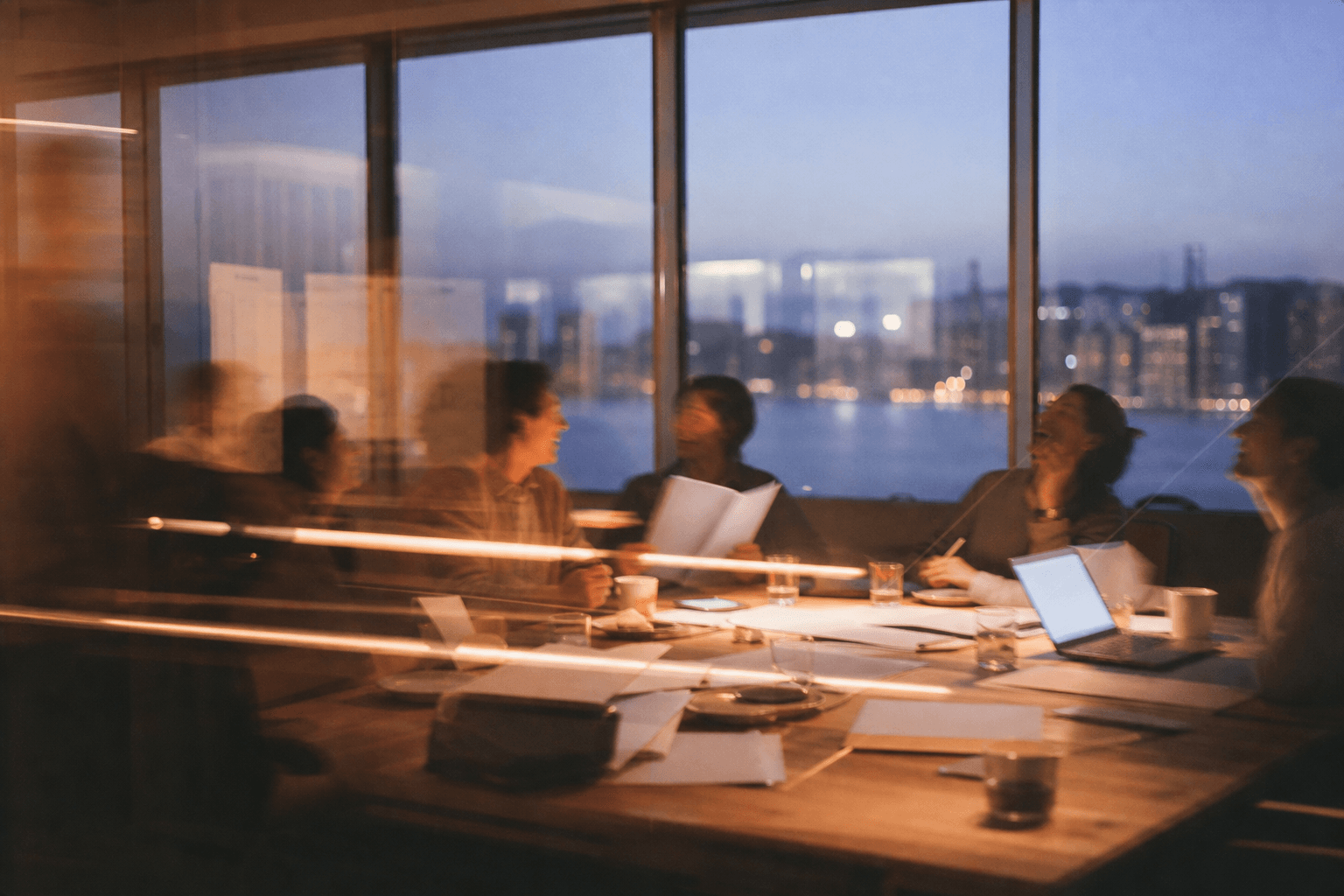 A team reviews documents around a table at dusk, with a city view behind them