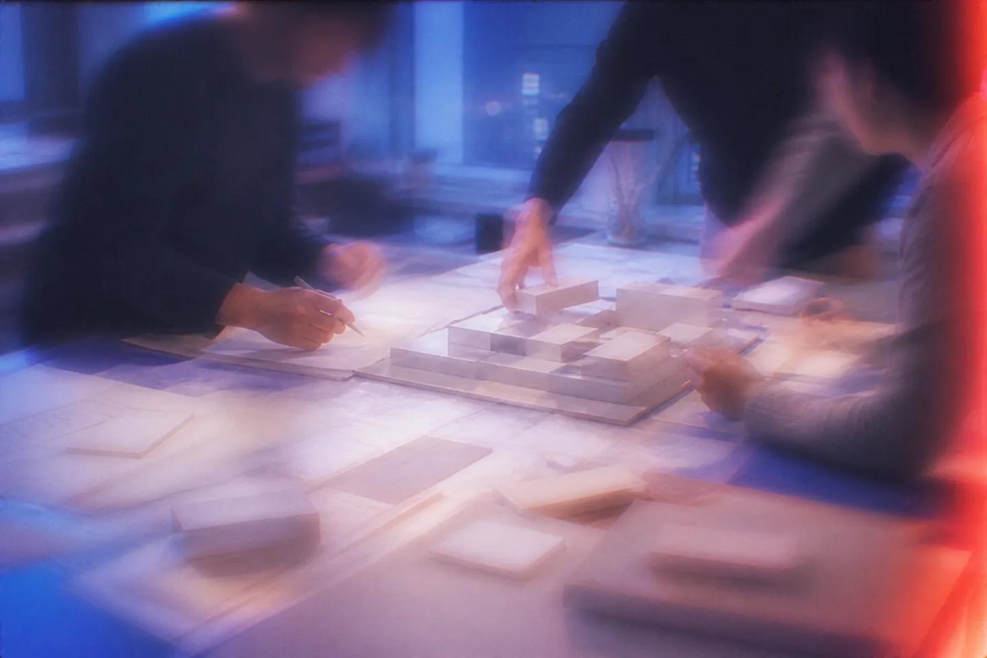 Hands shaping an architectural model around a shared table